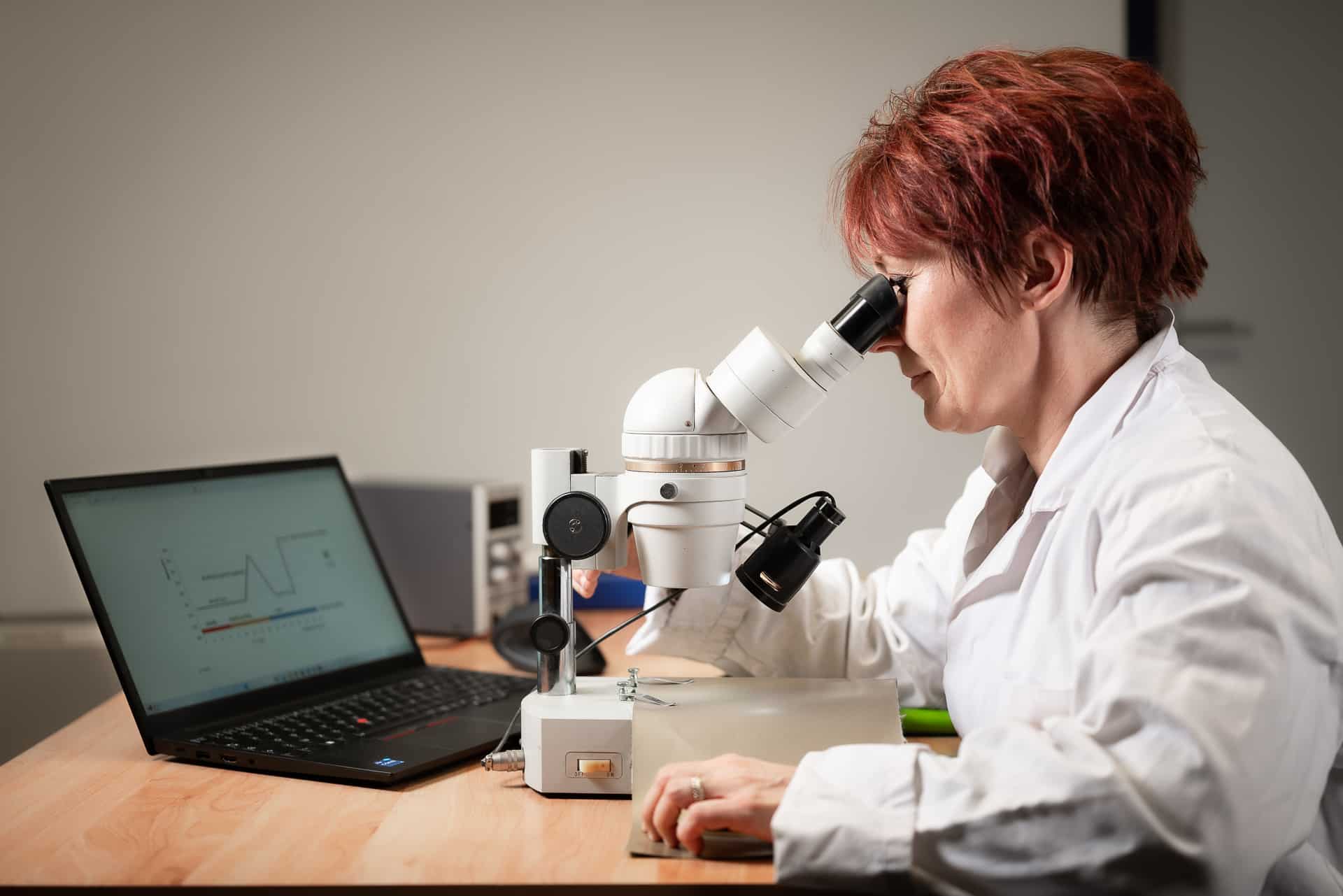 Una donna dai capelli rossi che guarda attraverso un microscopio con un computer davanti a lei